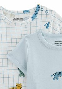 Deux t-shirts pour enfants : l'un blanc avec un motif à carreaux bleus et des motifs animaliers, l'autre bleu clair, tous deux en coton doux.