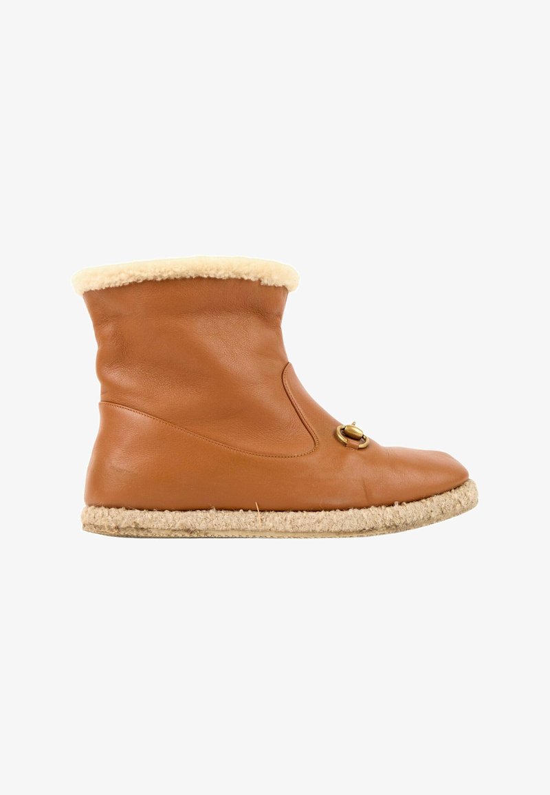 Bottine en cuir marron avec doublure et semelle en laine beige, avec une boucle décorative dorée sur le côté.
