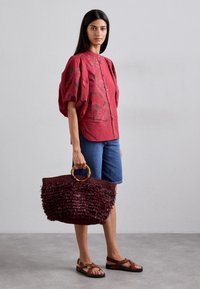 Piros virágmintás, gombos blúz puffos ujjal; farmer rövidnadrág; barna szandál; textúrált, rojtos burgundi táska kerek fogantyúval.