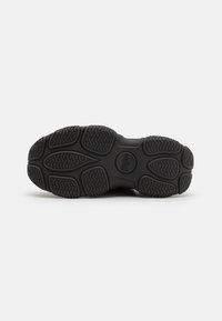 Black rubber sneaker sole with textured patterns, featuring thick tread for grip, and a round logo in the center.