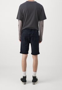 Shorts de mezclilla oscura con bajos enrollados, combinados con una camiseta gris y mangas largas estampadas, completados con zapatillas negras y calcetines blancos.
