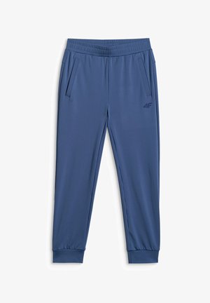 Enfant en tenue de sport bleue tenant un ballon de football sous un bras et une bouteille d'eau dans l'autre main, debout sur un fond gris.