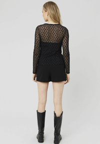 Haut noir à manches longues avec un dos en mesh transparent, présentant un motif floral. Associe à un short noir et des bottes noires jusqu'aux genoux.