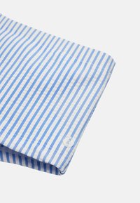 Puño de camisa de algodón con rayas azules y blancas, textura suave y un botón transparente con un logo en relieve.