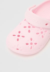 Rožu krāsas plastmasas ieģērbs ar ziedu izgriezumiem, noapaļota pirksta daļa un regulējams siksniņš. Strukturēta virsma ar gludu apdari.