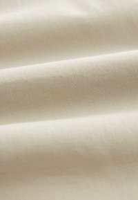 Smooth beige fabric with visible fine diagonal weave texture, shown in soft folds creating gentle shadows and highlights.