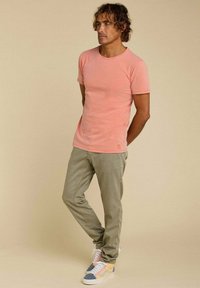 T-shirt rose clair à manches courtes, associé à un pantalon vert olive et des baskets multicolores. Design simple, texture douce.