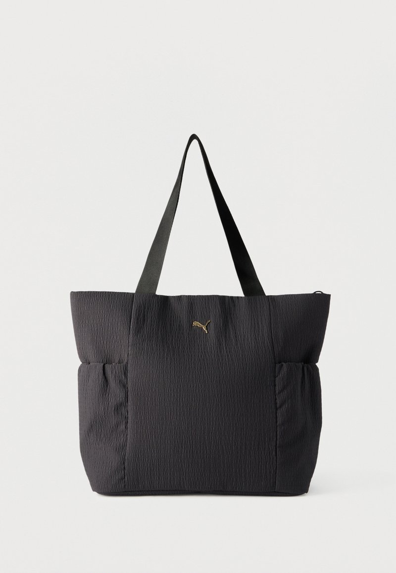 Sac fourre-tout texturé noir avec doubles poignées et poches latérales élastiques, arborant un petit logo Puma doré au centre avant.