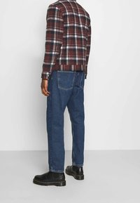 Giacca a quadri in tonalità bordeaux e bianco, abbinata a jeans blu e stivaletti neri. La texture è liscia, con una vestibilità su misura.