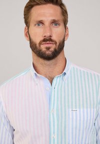 Camicia con bottoni caratterizzata da strisce pastello alternate in rosa e blu, con taschino sul petto e una consistenza morbida.