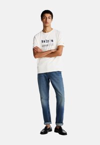 Maglietta bianca con stampa grafica, jeans blu con risvolti, e scarpe nere. Vestibilità casual e materiale in cotone. Design semplice con dettagli minimi.