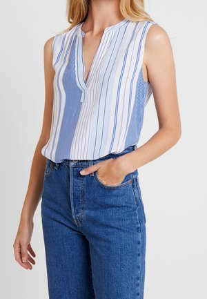 Blouse sans manches à rayures verticales bleues et blanches, avec un col et une patte de boutonnage cachée, associée à un jean en denim taille haute.