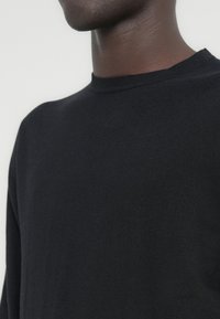 Pull noir à col rond en tissu doux, présentant une texture lisse et une coupe décontractée. Aucun motif ni embellissement visible.