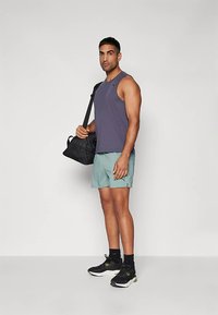 Top desportivo sem mangas roxo, calções verdes claros, sapatos desportivos pretos com pormenores amarelos, e uma mala de ginásio preta.