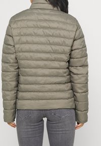 Olivgrön puffjacka med quiltad design, hög krage och elastiska muddar, med en mjuk textur och lätt konstruktion.