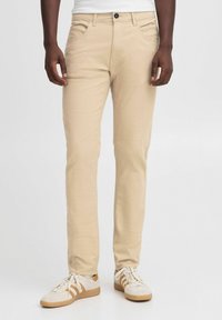 Pantaloni in misto cotone beige con vestibilità slim, cinque tasche e chiusura con bottone. Indossati con sneakers bianche con dettagli in marrone.