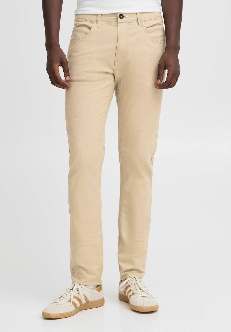 Pantaloni in misto cotone beige con vestibilità slim, cinque tasche e chiusura con bottone. Indossati con sneakers bianche con dettagli in marrone.