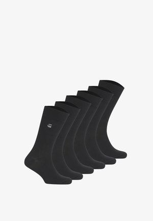 Sechs Paare schlichte schwarze Knöchelsocken, in einer Reihe angeordnet, jeweils mit einem kleinen grauen Logo nahe der oberen Manschette.