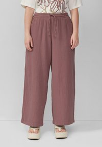 Wide-leg broeken in een stofkleur met een gedempte rozetint, vervaardigd uit textuurstof met een verstelbare tailleband. Gecombineerd met lichtgekleurde platform sandalen.