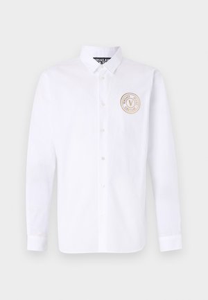 Biała, długoszeregowa koszula z bawełny z kołnierzykiem zapinanym na guziki. Posiada okrągłe, beżowe logo po lewej stronie klatki piersiowej. Klasyczny krój z zapięciem na guziki.