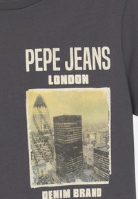 Szara bawełniana koszulka z nadrukiem graficznym londyńskich budynków oraz napisem „Pepe Jeans” w pogrubionych białych literach. Wzór ma teksturowany, vintage wygląd.