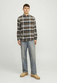 Bruin en wit geruit overhemd met lange mouwen en knopen, gecombineerd met lichtblauwe jeans en beige schoenen. Eenvoudig ontwerp met een klassieke pasvorm.