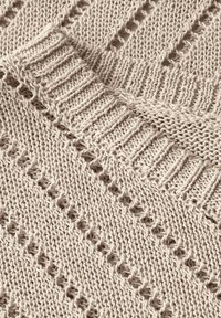 Beige knitted fabric featuring a textured pattern with open and closed stitches and a ribbed neckline. Soft and lightweight material.