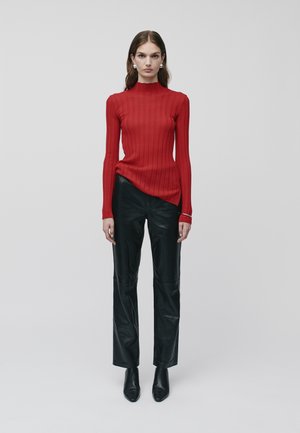 Roter gerippter Rollkragenpullover mit langen Ärmeln, kombiniert mit schwarzen Lederhosen und spitzen Ankle Boots. Schlichtes und figurbetontes Design.