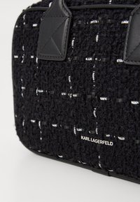 Sac à main noir texturé avec un motif tressé affichant le texte "KARL LAGERFELD" et des poignées en cuir noir.