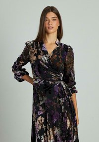 Vestido envolvente negro con estampado floral, acentos en púrpura y dorado, mangas largas, escote en V profundo y cintura con lazo. Tejido transparente con patrones florales texturizados.