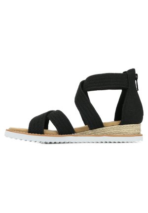 Sort åben tå kile-sandal med vævede stofstropper, tan polstret indersål, flettet mellemsål, hvid tekstureret gummiydersål og lynlås bagpå.