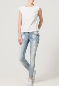 White textured short-sleeve top with a round neckline, paired with light blue distressed skinny jeans and white sneakers.
