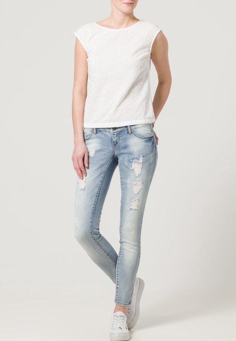 White textured short-sleeve top with a round neckline, paired with light blue distressed skinny jeans and white sneakers.