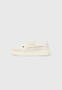 White sneaker with mesh and suede materials, round toe, lace-up front, low profile, and logo accents on the side and tongue.