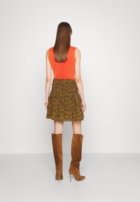 Haut sans manches orange à côtes associé à une jupe noire ornée de motifs floraux jaunes. Bottes en suède marron jusqu'aux genoux avec des pointes.