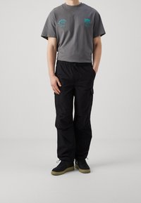 Szara bawełniana koszulka z krótkim rękawem, z turkusowym napisem; w połączeniu z luźnymi czarnymi spodniami cargo; czarne trampki z gumową podeszwą.