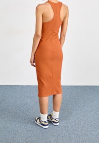 Hnědo-oranžový žebrovaný midi šaty s designem na závodním zádech, s upnutým siluetou. Nosit s bílými ponožkami do sportovních bot a modrými teniskami.