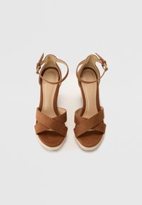 Sandali con tacco in suede marrone, con cinturini incrociati, fibbia alla caviglia e piattaforma in espadrilles texturizzate. Fodera interna liscia e design con punta aperta.