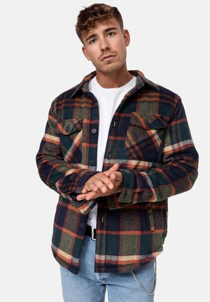 Flannel shirt in navy, green, and rust plaid. Features two chest pockets, button closure, and a collared neck. Soft texture.