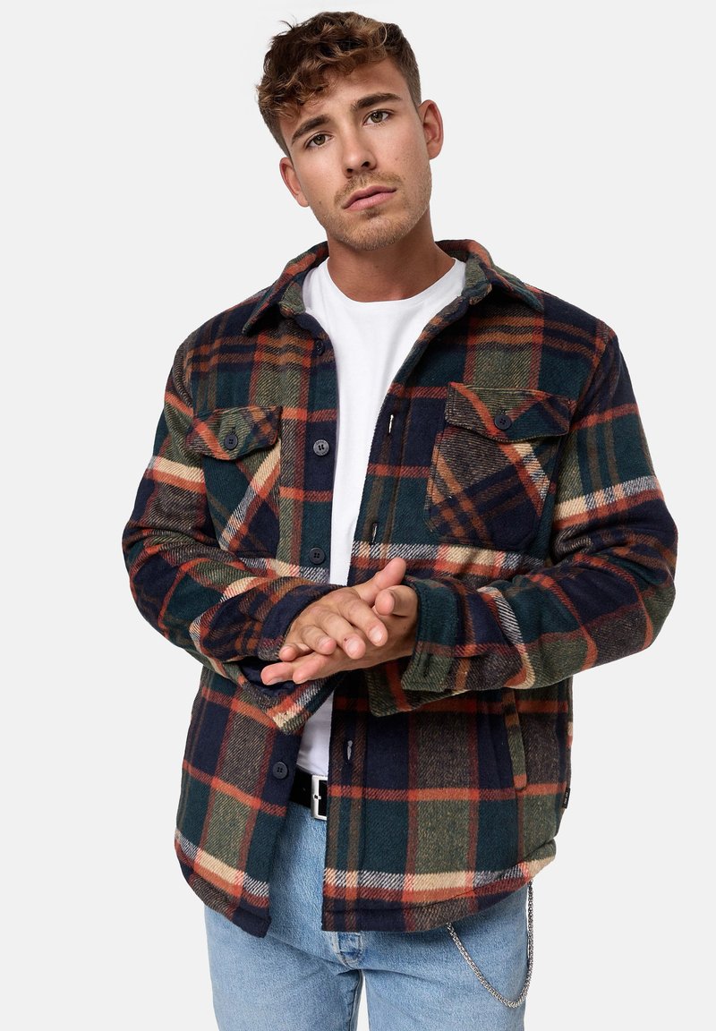 Camisa de franela en cuadro de color marino, verde y óxido. Cuenta con dos bolsillos en el pecho, cierre de botones y cuello. Textura suave.