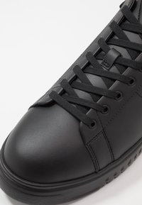Black leather sneaker with flat black laces, rounded toe, and perforated sole. Features seamless design and a matte finish.