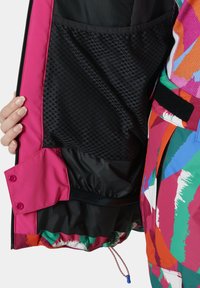 Kleurvolle binnenkant van de jas met een roze schuiling, een zwart gaaszakje en levendige abstracte patronen, voorzien van een koord en klittenbandsluitingen.
