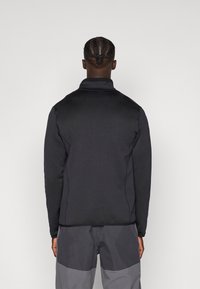 Zwart fleece jack voor mannen met een hoge kraag, een getailleerd ontwerp en een soepele textuur. Inclusief tonale stiksels en een volledig achteraanzicht.