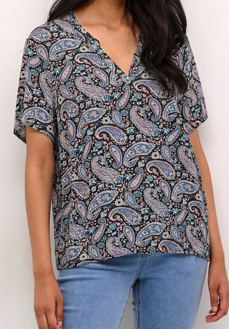 Sort top med paisley-mønster i blå, pink og hvid. Kortærmet med V-hals design. Glat stoftekstur. Båret med lyseblå jeans.