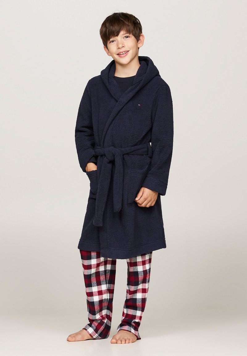Navyblauwe fleece badjas met een capuchon en riem, voorzien van twee voorzakken. Rood-witte geruite pyjamabroek maakt de outfit compleet.