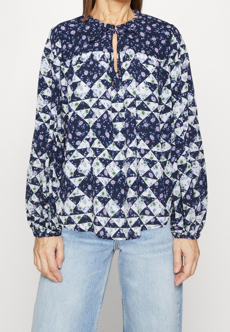 Langsleeve blouse met een marineblauwe bloemenpatchwork ontwerp met vierkante en driehoekige vormen, een keyhole hals en elastische manchetten.