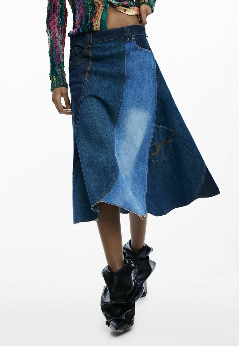 Jupe en denim aux nuances variées de bleu, avec un ourlet asymétrique et une poche plaquée. Associée à des bottes noires décontractées.