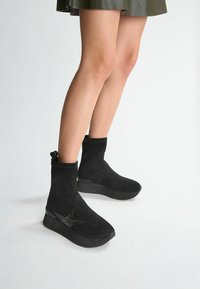 Stivaletti alla caviglia in suede nero con un design elegante, caratterizzati da un accento a forma di stella lucida, un polsino elastico e una suola in gomma spessa.