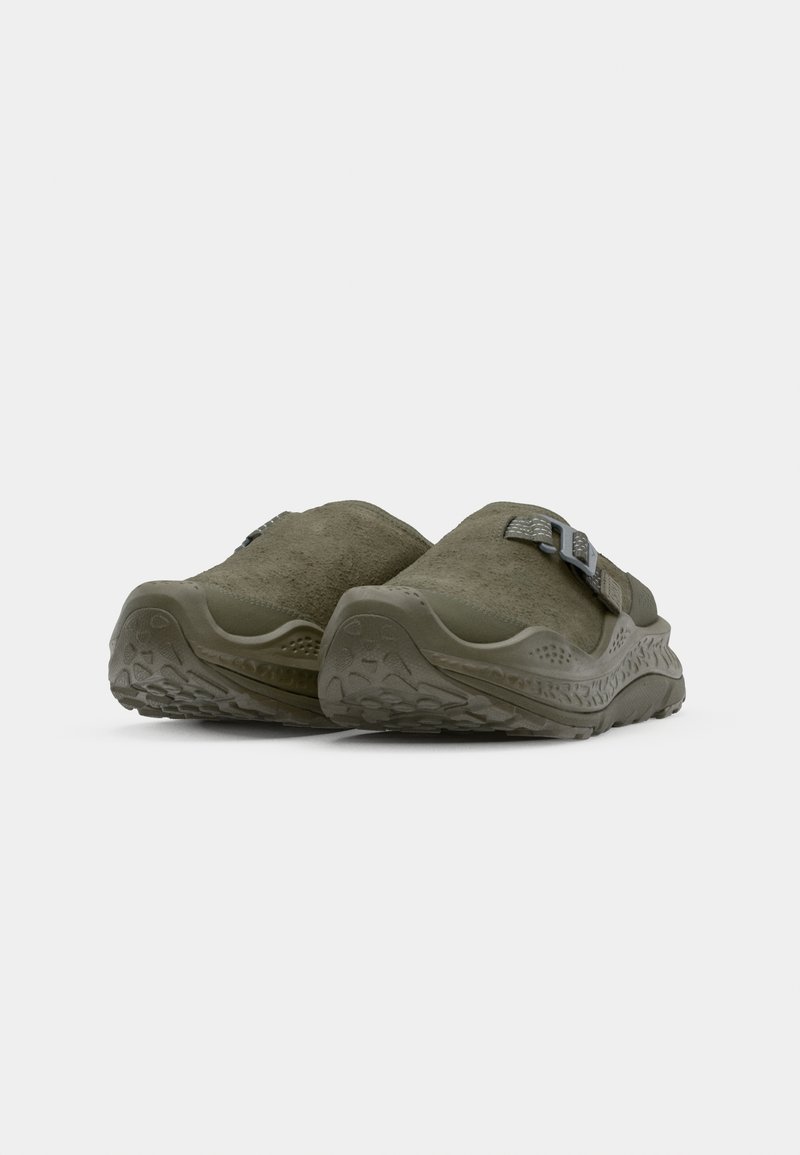 Olive green slip-on shoes with suede upper, textured rubber sole, and adjustable buckle detail. Rounded shape and cushioned design.
