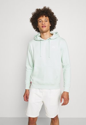 Mintgrüner Hoodie mit Kordelzügen, Fronttasche und dezentem Logo. Weicher Stoff, gerippte Bündchen, kombiniert mit weißen Shorts.